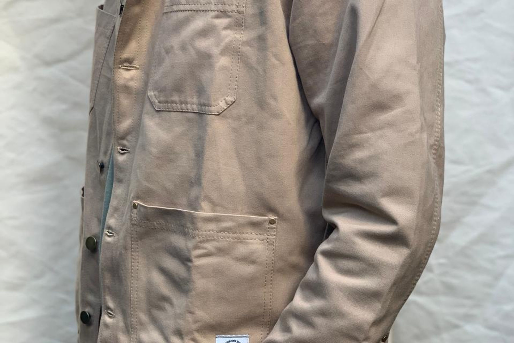 The sand canvas Chore Jacket up close: squared chest pocket, metal shank buttons and a riveted hip pocket.