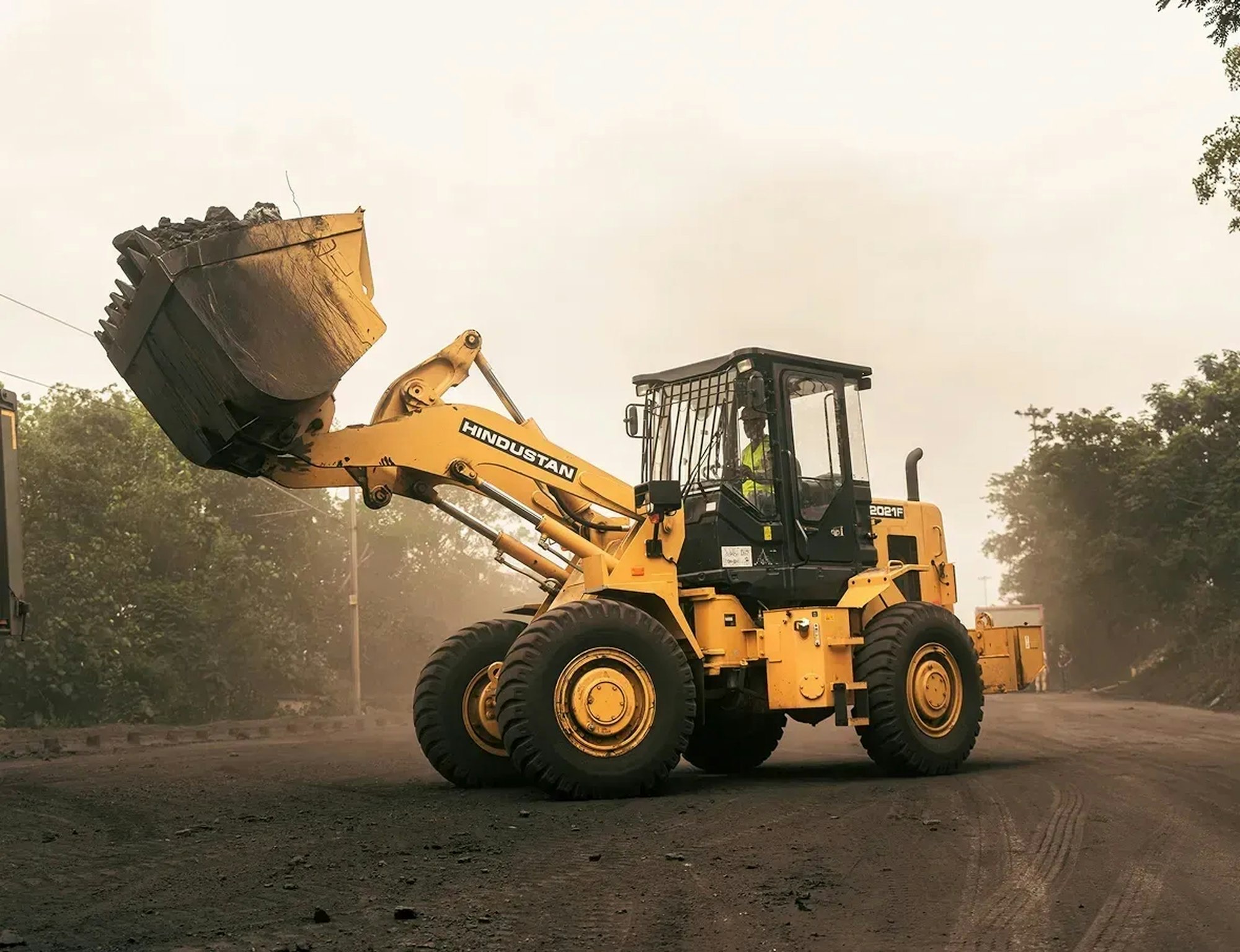 A front-end loader carrying earth along a dusty site road.