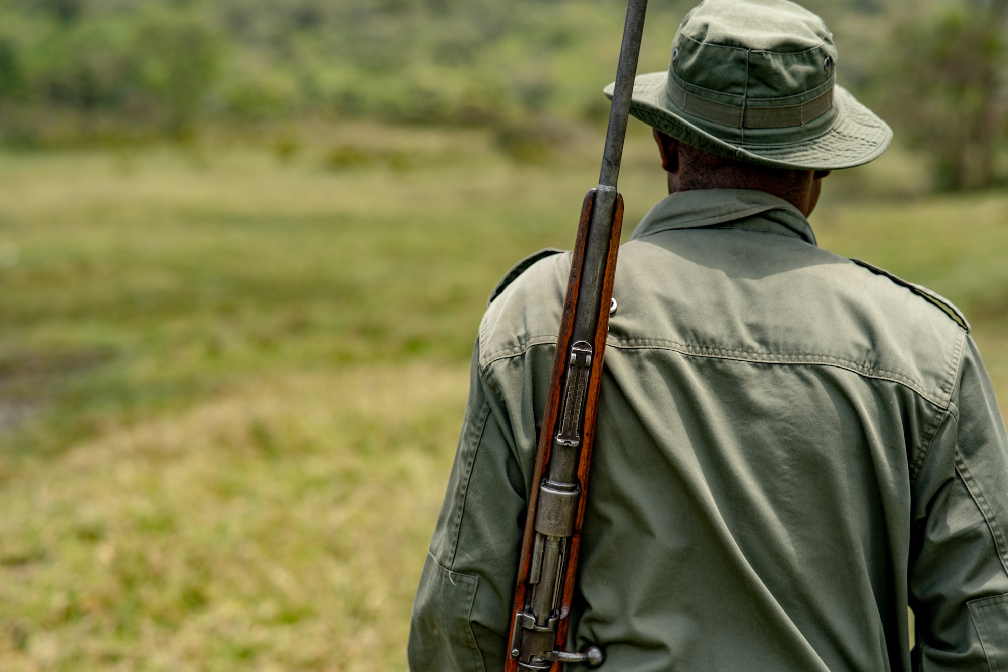 A game ranger in an olive field shirt and bush hat looking out over open savanna.